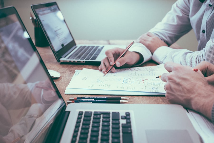 A picture of two men sitting at a desk with open laptops but still using pens and paper. This is how we start all of our website designs